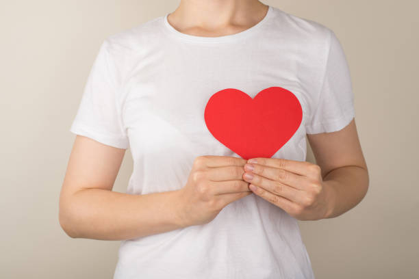 고립 된 회색 배경에 심장 근처에 빨간 종이 심장을 들고 흰색 티셔츠를 입은 젊은 여성의 크롭 클로즈업 사진 - human cardiovascular system heart shape human hand healthy lifestyle 뉴스 사진 이미지