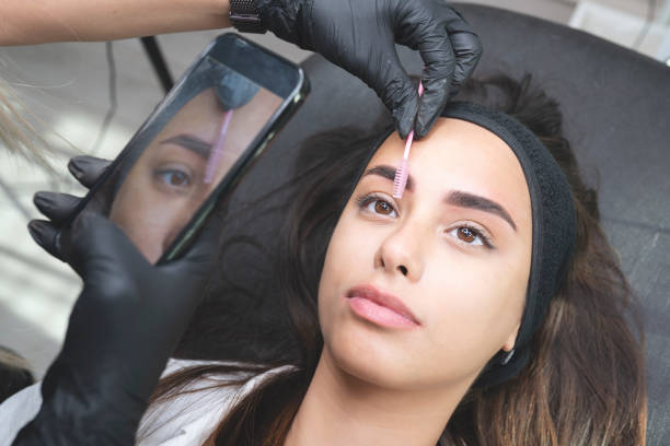 Beautician is applying permanent make up Beautician is using a eyebrow brush and taking a photo with smart phone. Beautiful young woman in beauty salon on eyebrow makeup treatment. Beautician doing eyebrows tattooing. Ruler permanent marker photos stock pictures, royalty-free photos & images