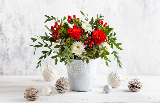 Festive winter flower arrangement with red roses, white chrysanthemum and berries in vase on table. Christmas flower composition for holiday.