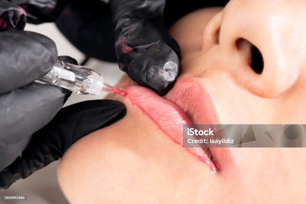 Beautician is applying permanent make up Beautiful young woman in beauty salon on lip makeup treatment. Beautician doing lips tattooing. Permanent Make-Up Stock Photo
