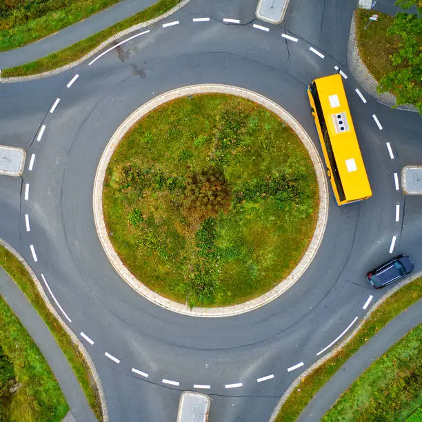 Abstract aerial view of traffic circle with yellow bus and black car vertically from above