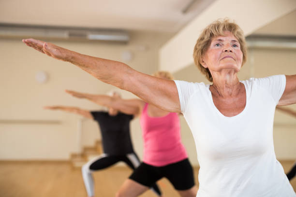 istock Elderly woman practicing Virabhadrasana during group yoga training 1345995503