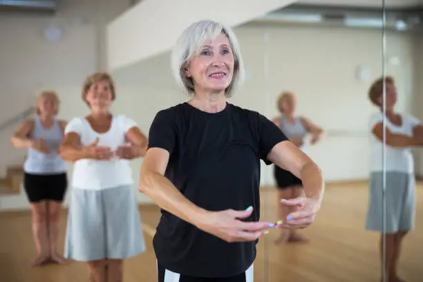 Photo of Mature woman practicing classic dance moves during group class