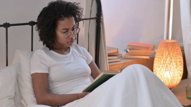 istock Young African Woman Reading Book in Bed 1345997661