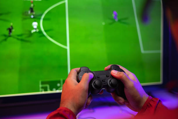 rückansicht junger player videocomputer pc. junger mann sitzt auf dem stuhl in der spielstation und hält den joystick. streamer-mann mit kopfhörern beim fußballspiel online in der dunkelkammer. - multiplayer stock-fotos und bilder