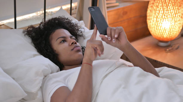 istock Smartphone use by Young African Woman Laying in Bed 1345998019