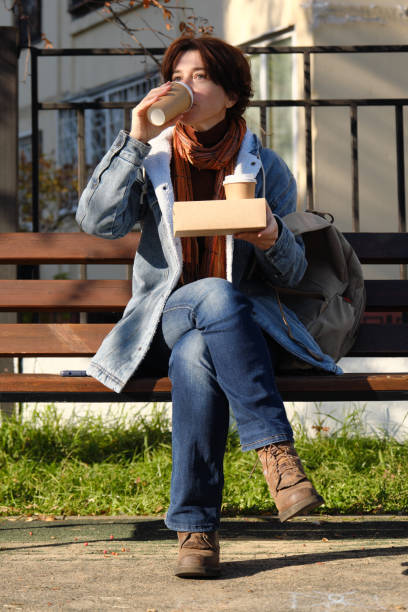 istock Mature woman is drinking coffee while waiting for someone on park bench 1345998201