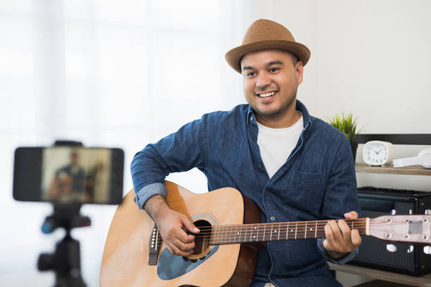 Young asian musician teaching the guitar class online live streaming with smartphone with student. Indian man playing acoustic guitar while singing a song and record by cell phone shaed online social joven músico asiático que enseña la clase de guitarra en línea transmisión en vivo con teléfono inteligente con el estudiante. hombre indio tocando la guitarra acústica mientras canta una canción y graba por teléfono celular shaed online social