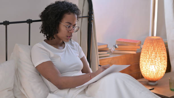 istock Young African Woman Reading Documents in Bed 1345999566