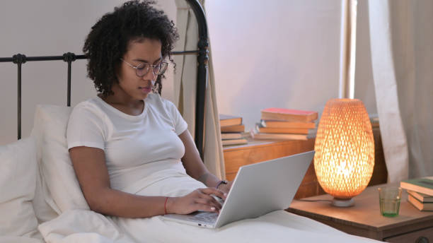 istock Young African Woman working on Laptop in Bed 1345999670