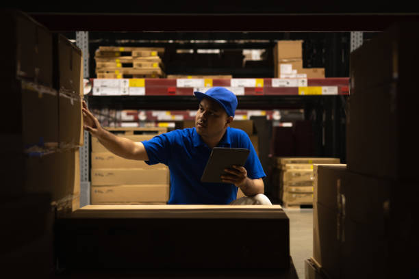 istock Young worker in blue uniform checklist manage parcel box product in warehouse. Asian man employee using tablet working at store industry. Logistic import export concept. 1346000828