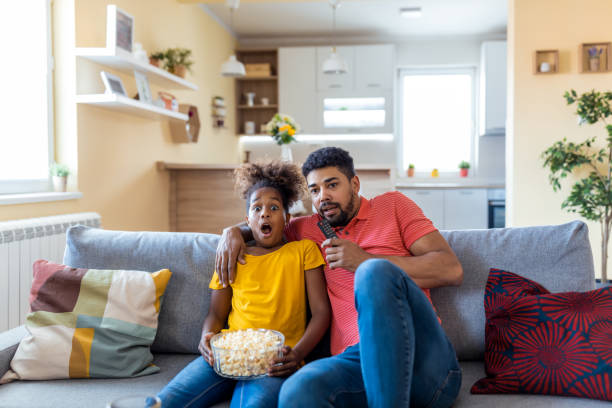 istock Father and daughter watching horror and eating popcorn, home interior 1346005036