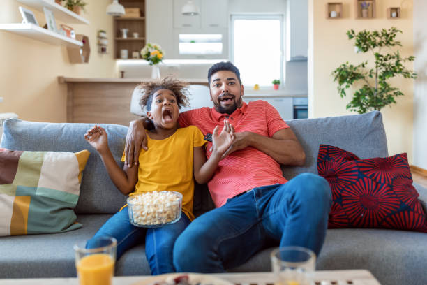 istock Father and daughter watching horror and eating popcorn, home interior 1346005039
