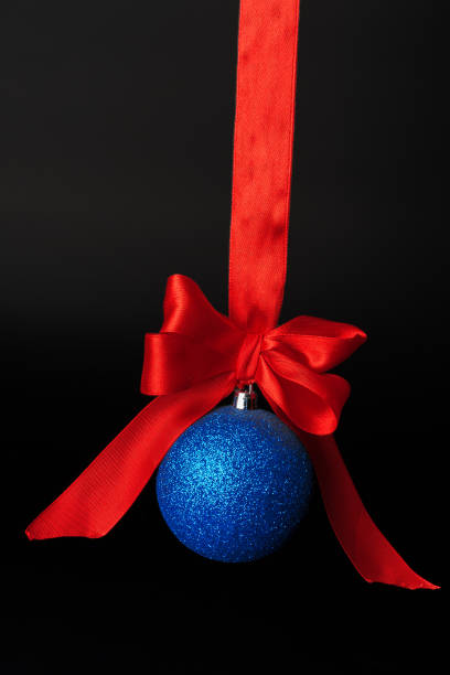 istock Christmas bauble hanging on red satin ribbon against black background 1346007444