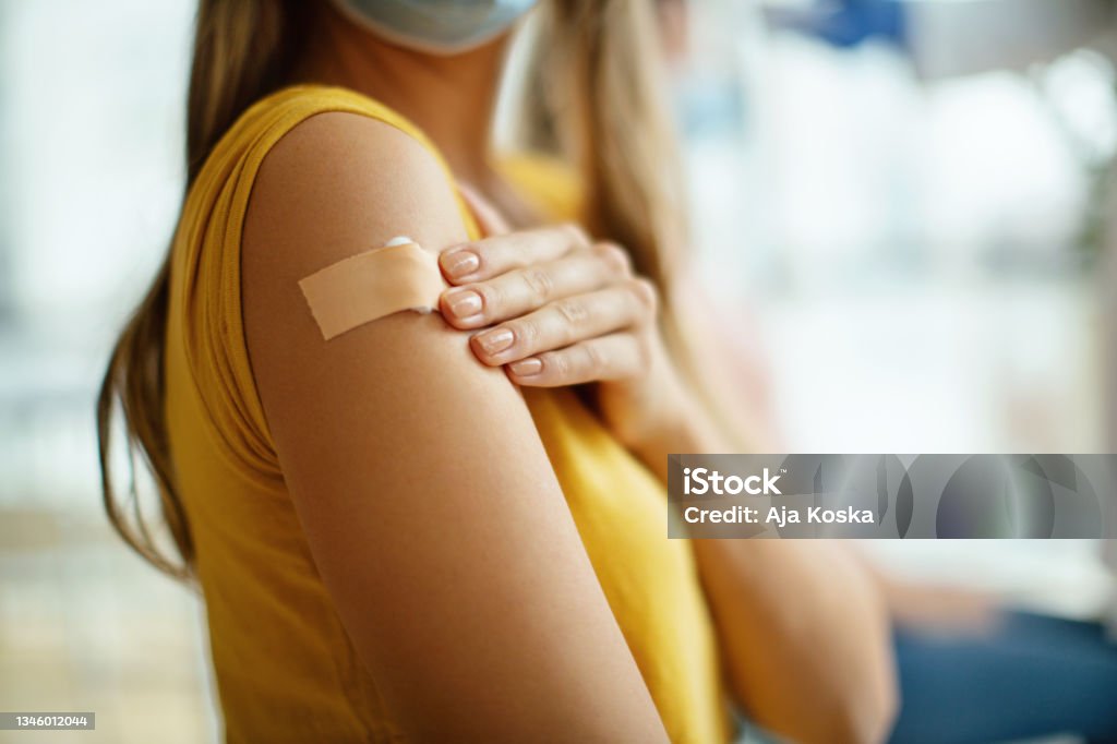 Covid-19 vaccination. Doctor had just vaccinated a young unrecognizable female patient in the hospital. She is pleased with how it all went.  Focus on adhesive bandage. Vaccination Stock Photo