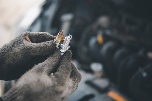 lavoro di sostituzione della candela, mano del meccanico d'auto che tiene la vecchia candela sull'auto con motore sfocato sullo sfondo. - spark plug electrode transportation workshop foto e immagini stock