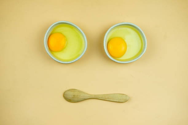 Raw egg in the small white bowl and wood spoon. Face funny shape, Top view