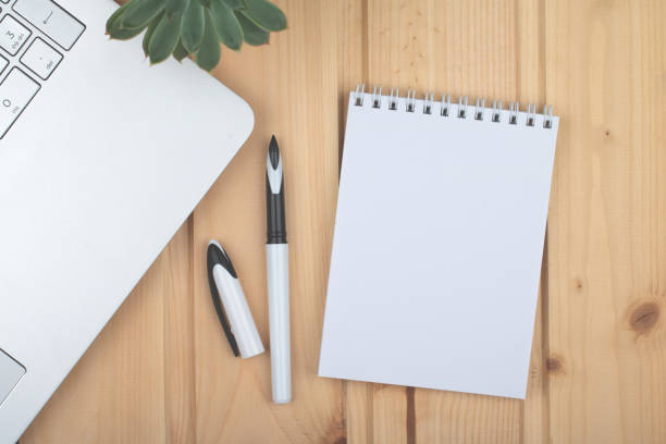 istock Clean notepad, laptop, pen, on wooden surface. 1346014002
