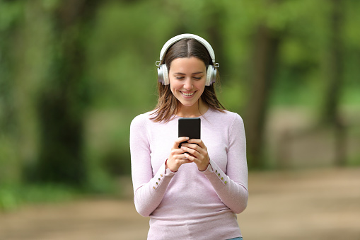 Happy woman walking listening to music on phone in a park