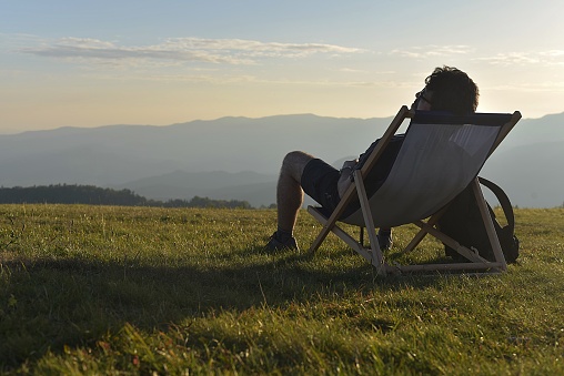 Man sitting on top of a hill on a decay-lounger and watching the sunset