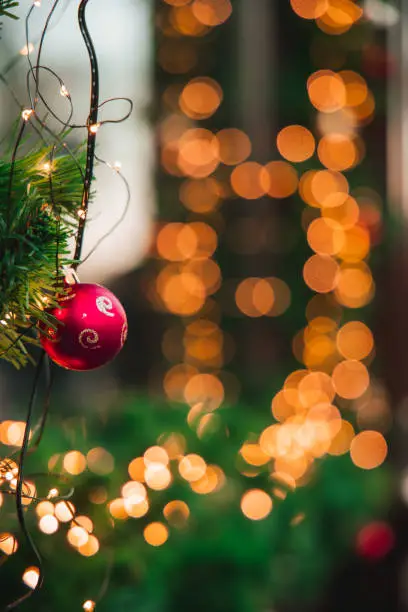 Photo of Christmas festive street and background vibrant bokeh lighting from garland lamps New Year eve time, unfocused foreground and background, focus on decorative ball on branch, vertical photo