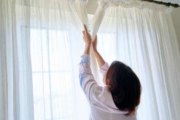 Close-up of woman's hand opening and closing light translucent curtains stock photo