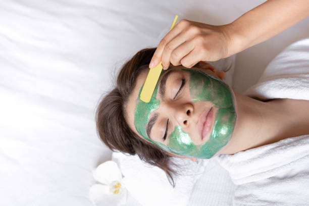 젊은 여성의 얼굴에 녹색 화장품 마스크를 적용하는 과정. - clear sky human skin towel spa treatment 뉴스 사진 이미지