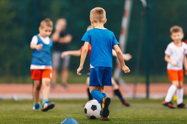 学校のフィールドでサッカーの試合をするハッピ�ースクールの子供たち。人工芝場でサッカーボールを蹴る少年たち - 子供サッカー ストックフォトと画像