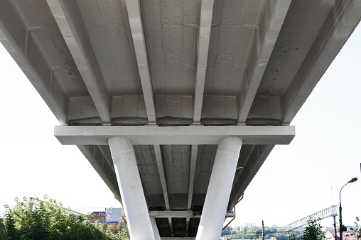 Construction of concrete road bridge supported by pillars, viewed from the bottom up. Under the bridge, perspective.