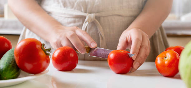istock Chef slicing tomato using knife on the table in restaurant. Process of cutting and preparation food in kitchen. 1346027643