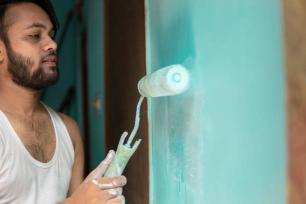 Indian man painting house wall with a paint roller.