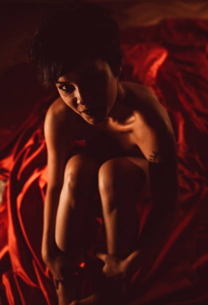 femme recroquevillée sur des draps rouges - passion people love sensuality photos et images de collection