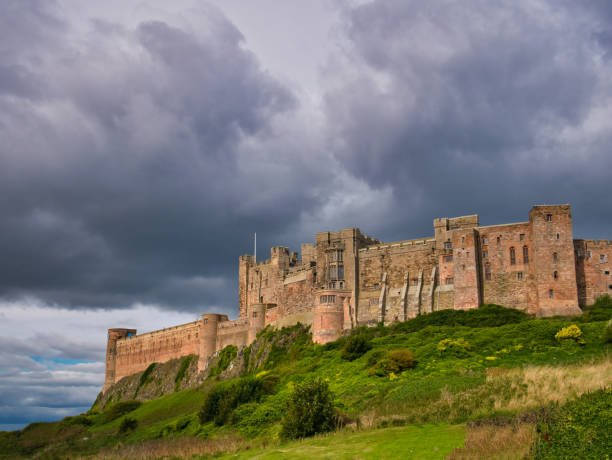 영국 북동부 노섬버랜드의 밤버그 성(bamburgh castle)의 1학년 건물의 요새같은 남서쪽 면인 위협적인 구름속에서 태양이 빛나고 있습니다. - castle bamburgh northumberland england bamburgh castle 뉴스 사진 이미지