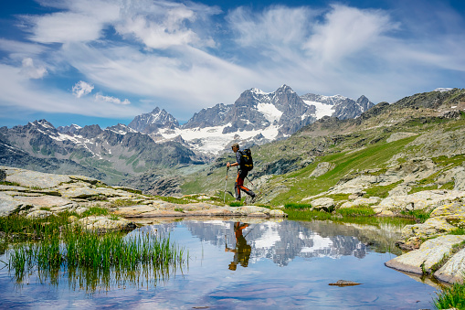Hiker across a mountain lake. Sky, mountain and hiker reflecting in the lake