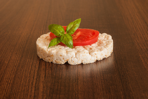 Rice waffle with tomato slice and green basil leaf on a solid wooden table. A healthy, vegetarian snack. Simple breakfast.
