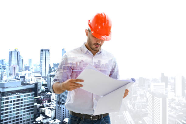 istock Double exposure image of construction engineer manager workers in orange hardhat and looking layout plan standing during overlay with construction site in the city. 1346033912