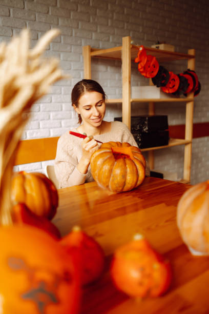 istock Young woman cutting with knife character face on pumpkin object preparation to halloween holiday. 1346034026