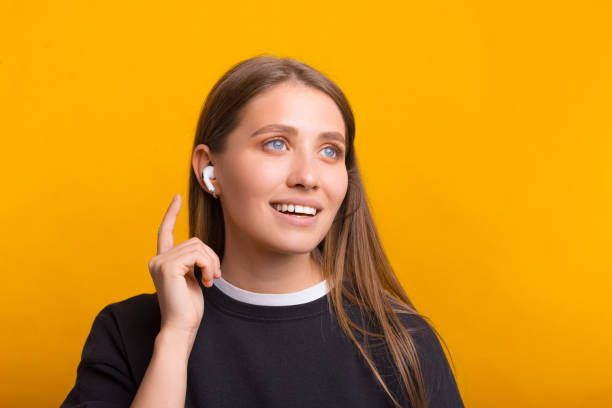 Beautiful woman is wearing some wireless ear pods over yellow background. stock photo
