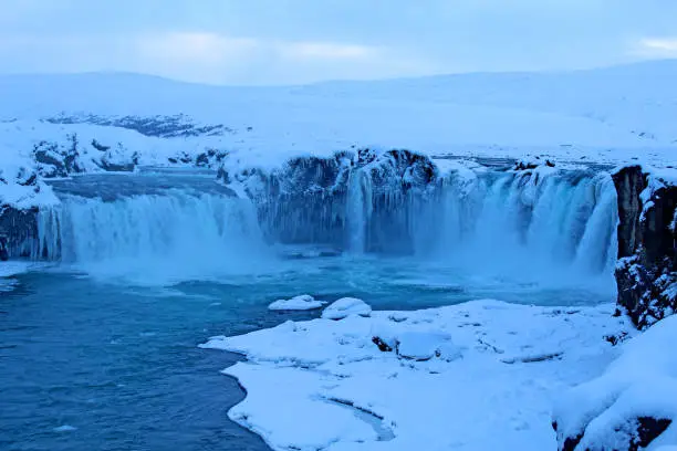 Goðafoss is a waterfall in northern Iceland. This winter picture is filled with snow and icicles. It is blue and brutally cold  next to the waterfall.