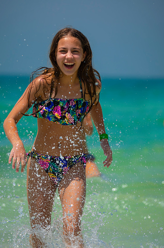 Cute Teen Girl Runs Out of the Sea on the Beach. Splashing the Water and Laughing. Happy Summer Vacation on the Beach Resort.