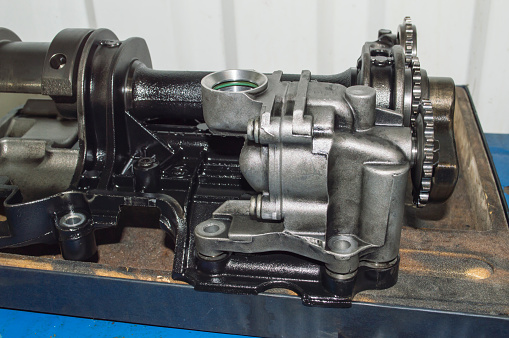 A side view of the oil pump of an automobile internal combustion engine with balancing shafts lies on a work table in an auto repair shop