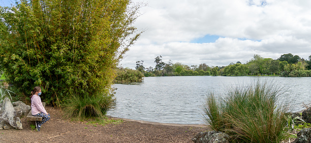 Young Girl Sitting on Bench in the Park in Front of a Lake - Panorama with copy space