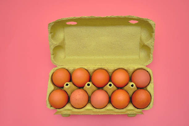 A full package of brown eggs in a cardboard box on a pink background
