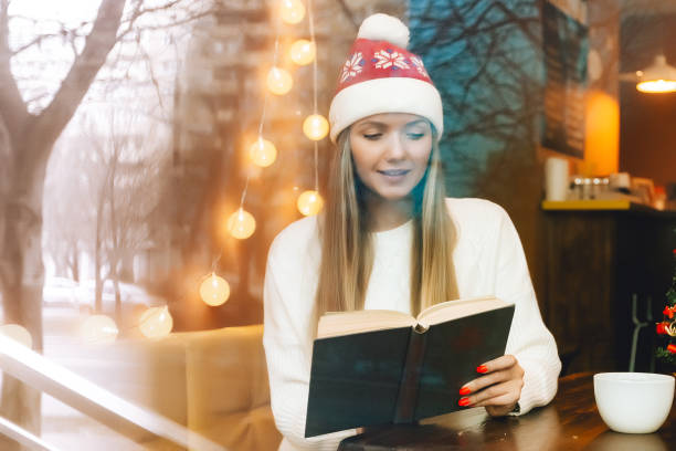 カフェで本と飲み物とガラス窓の後ろにクリスマス帽子の素敵な女性。新年の気分。 - broken window glass women ストックフォトと画像