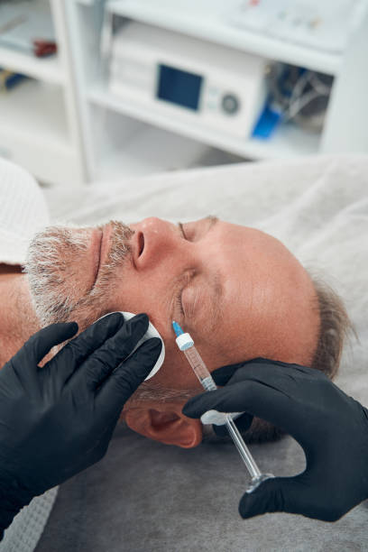 man having anti-aging injection procedure in cosmetology clinic - ogen dicht closeup vrouw 50 jaar stockfoto's en -beelden