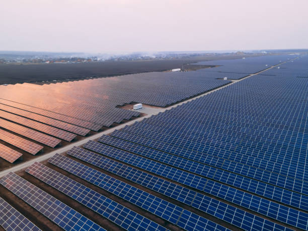 istock Aerial drone view into large solar panels at a solar farm at bright sunset. Solar cell power plants. 1346060803
