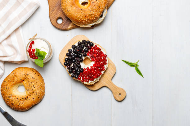 Sweet bagels with butter cream and fresh berries. On a wooden board. Overhead, horizontal, with space. Light, gray, wooden background stock photo