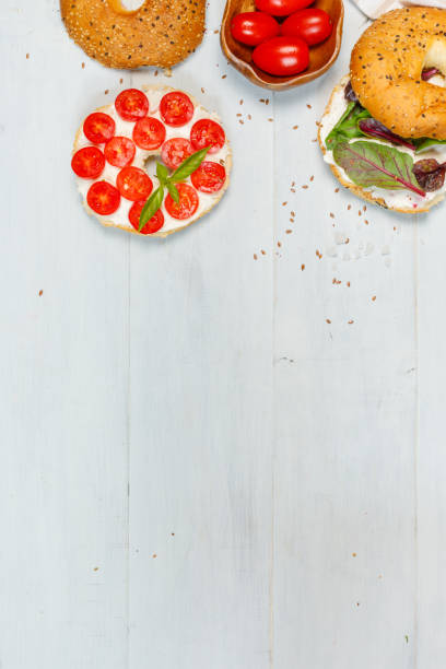 Open bagel sandwiches with cream cheese, sweet tomatoes and mixed salad. Top view, on a light wooden background. A copy of the space,vertical stock photo