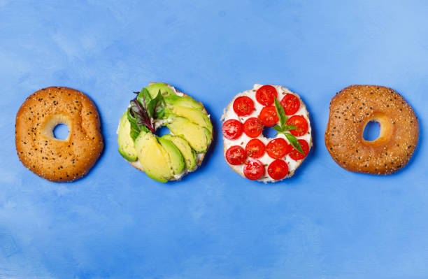 Bagels with different fillings on a blue background, top view. Bagel with tomatoes and avocado. Flat lay, horizontal stock photo