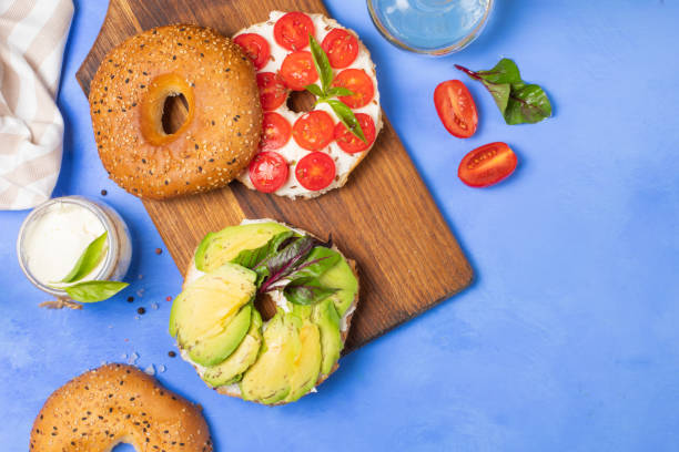 Bagel with cream cheese, tomatoes and avocado. On a blue background, horizontal, top view. Copy of the space stock photo